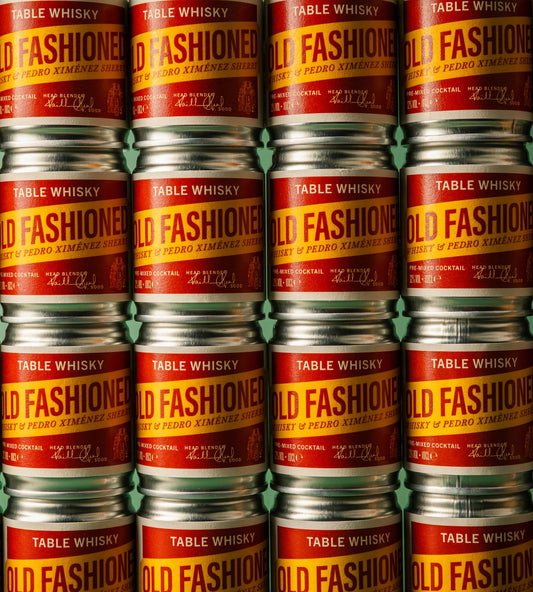 A tightly cropped view of stacked metal cans of Table Whisky, showing repeated labels that read "Table Whisky Old Fashioned, Whisky & Pedro Ximénez Pre-Mixed Cocktail".
