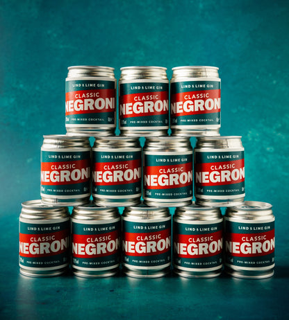 A pyramid arrangement of twelve metal cans of Lind & Lime Gin Classic Negroni cocktail on a textured teal background.