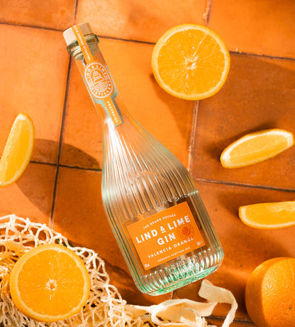 A bottle of Lind & Lime Gin Valencia Orange, styled on a terracotta tile background with fresh orange slices